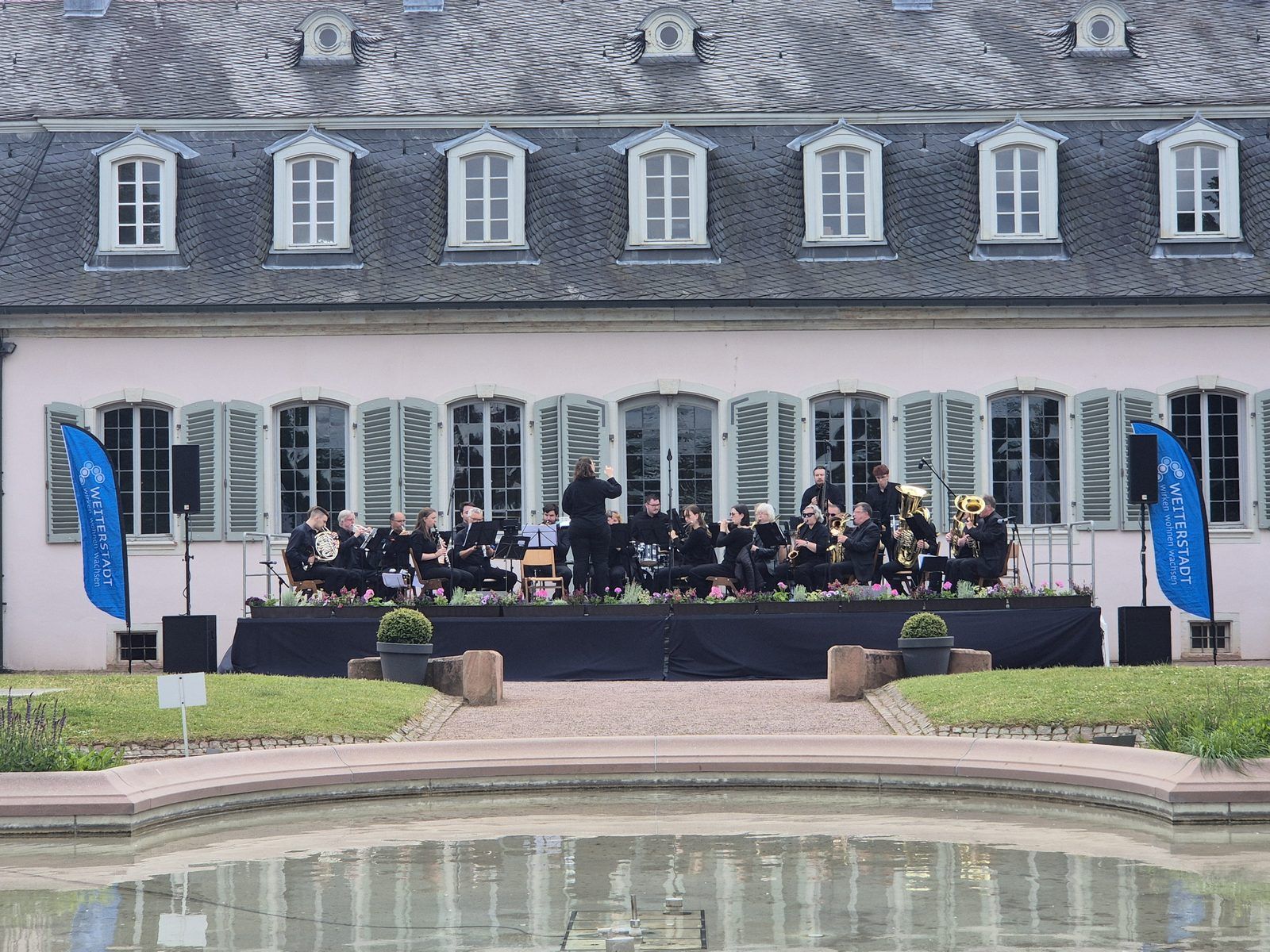 Das Blasorchester TSV Braunshardt spielt bei »Ein Park voller Musik« auf der Bühne vor dem Schloss Braunshardt, im Vordergrund der Weiher